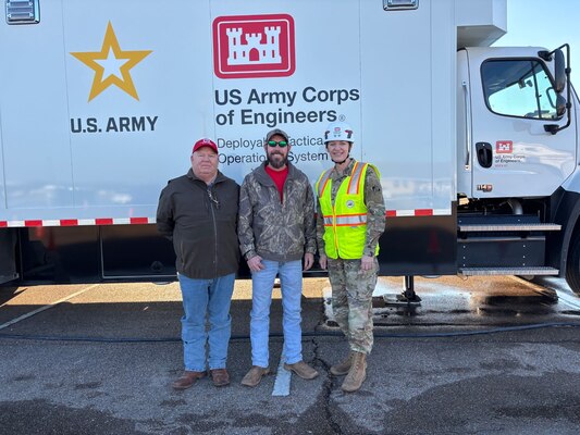 Two men and a female Soldier stand in front of a large vehicle.