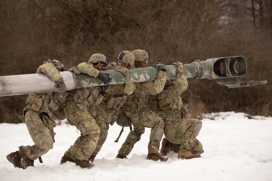 Five soldiers set up a weapon in a snowy field.