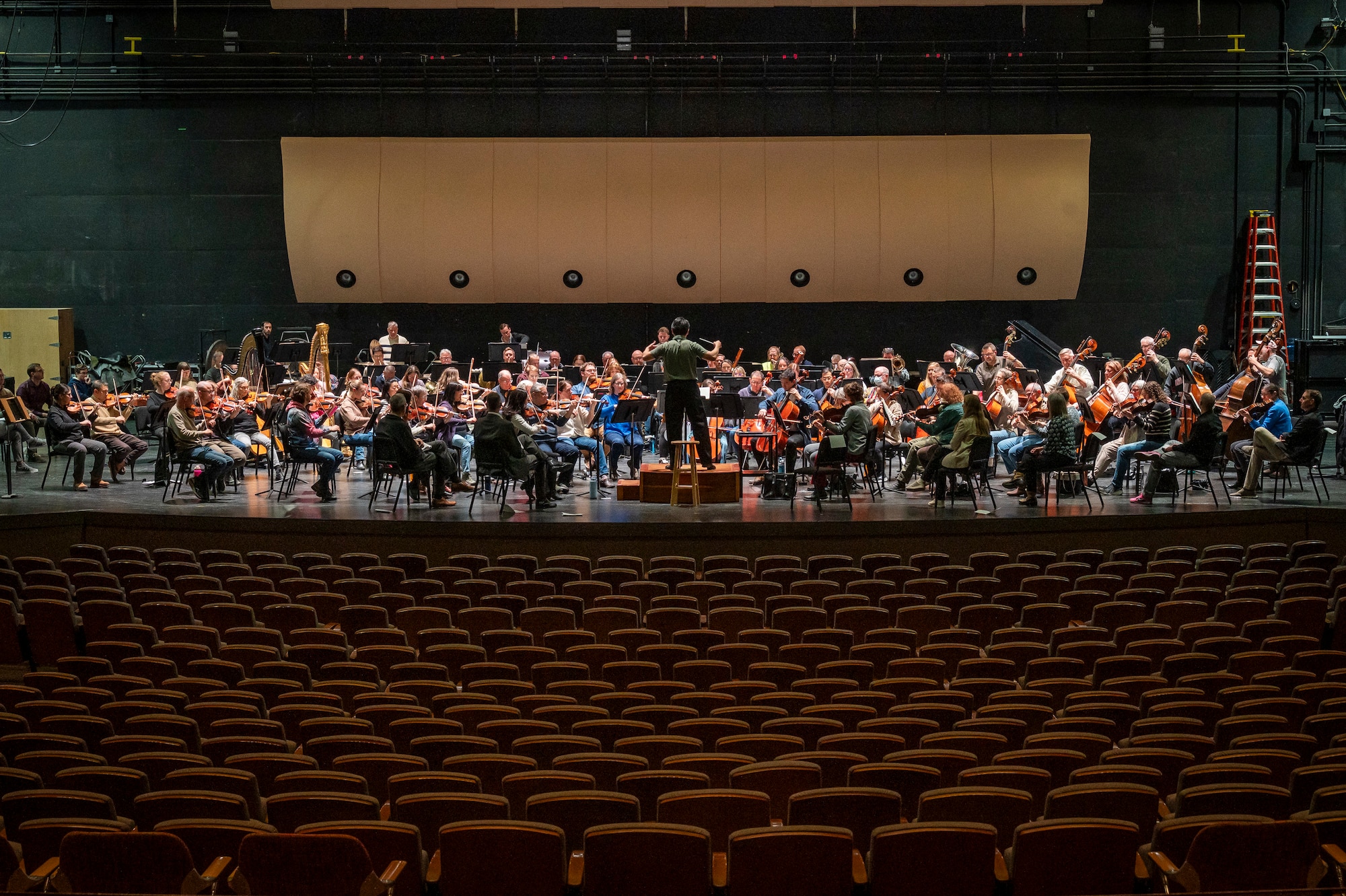 Members of orchestra practice on a large stage.