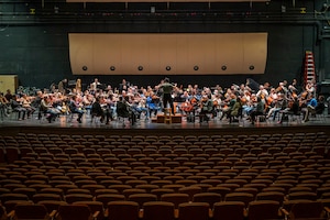 Members of orchestra practice on a large stage.