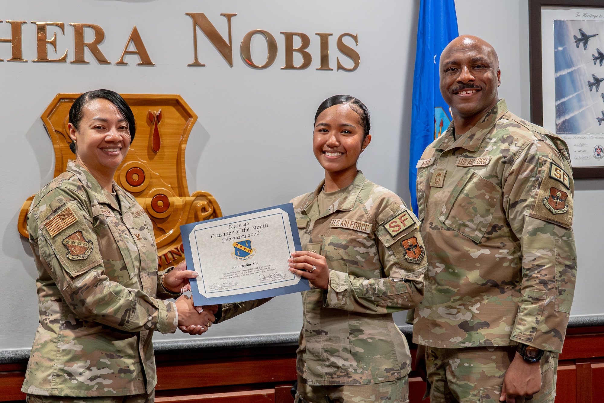 U.S. Air Force Col. Shamekia Toliver, 42d Air Base Wing Commander, and Chief Master Sgt. Eric Adams, 42d Security Forces Squadron senior enlisted leader, present Airman Destiny Mel, 42d SFS entry controller, the Crusader of the Month for February at Maxwell Air Force Base, Alabama, Feb. 4, 2026.