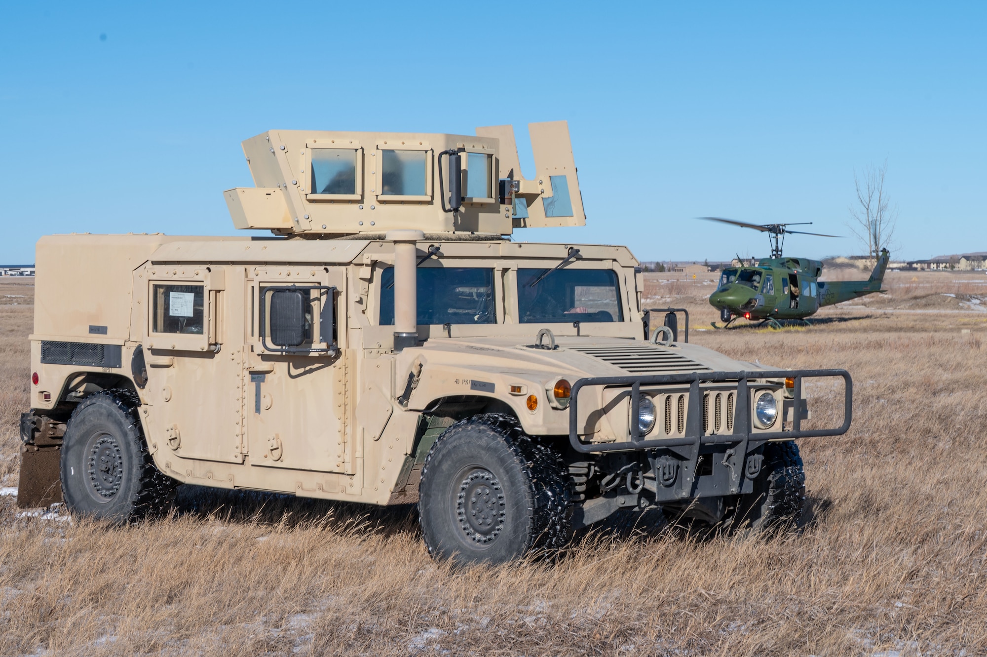 A Humvee parking in a field with a helicopter in the background.