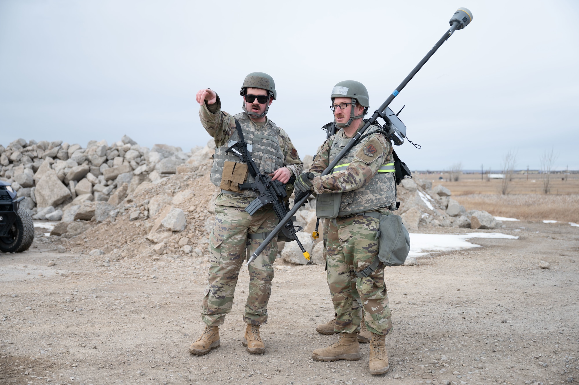 Two men in uniform at a construction site, one pointing into the distance and the other holding a pole.