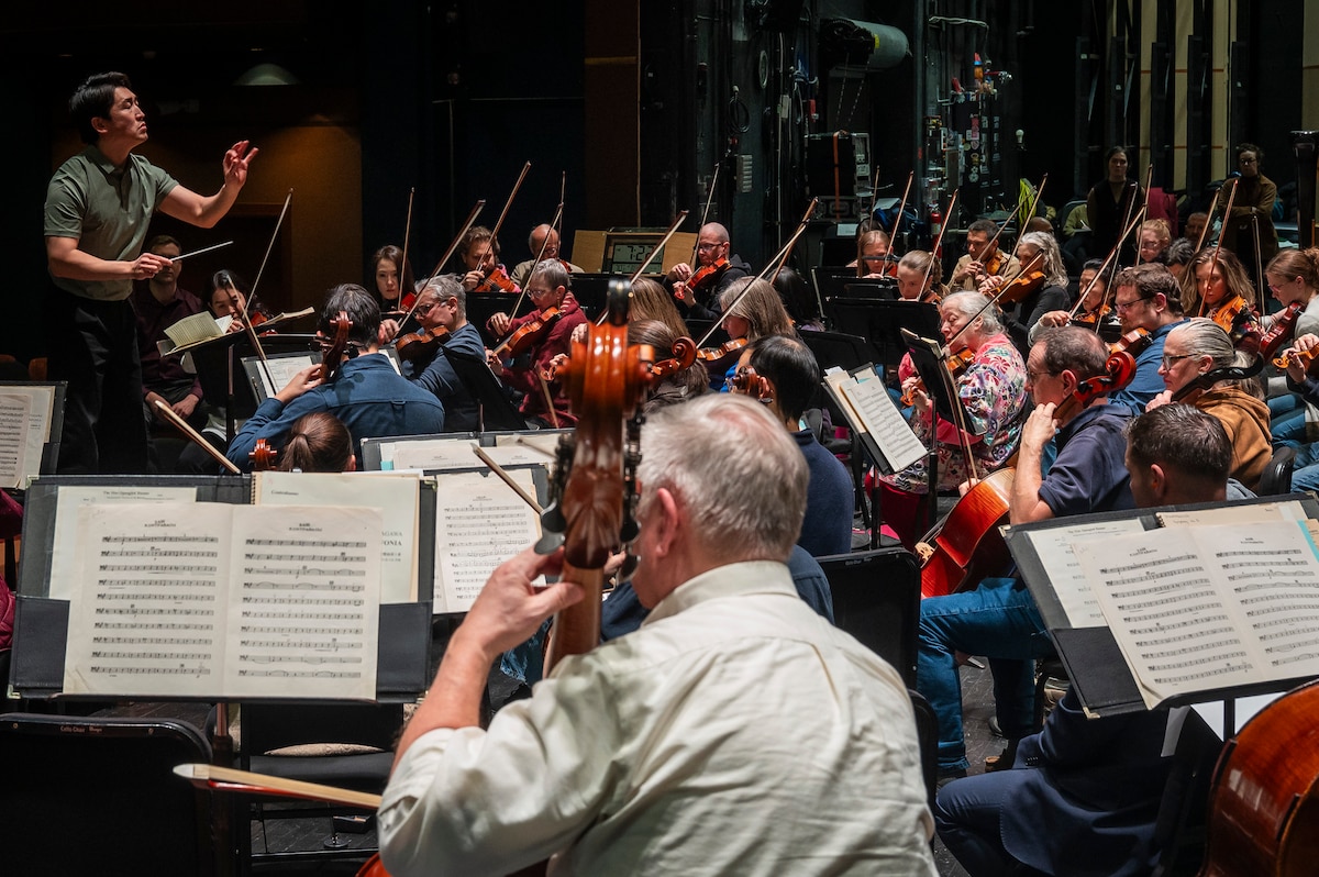 Closeup of orchestral musicians practicing. Conductor in background.