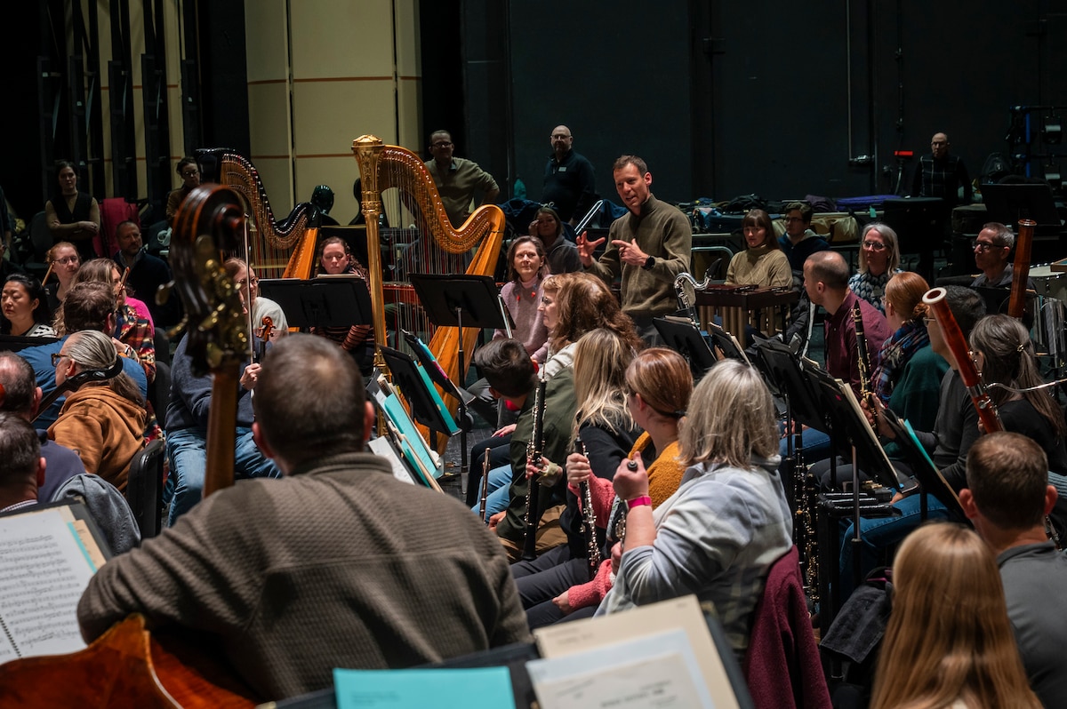 Orchestral musicians practicing on stage. Harp is visible.