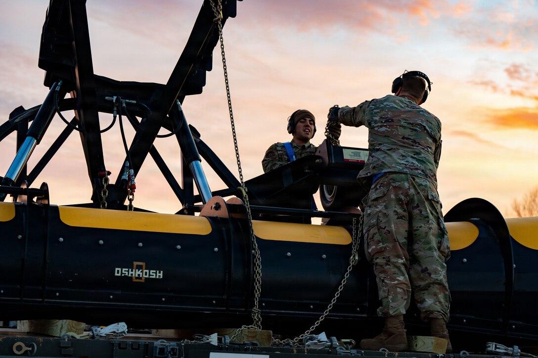 U.S. Air Force Airman 1st Class Alexander Monge, 89th Aerial Port Squadron aircraft services journeyman, receives a chain from Master Sgt. Tobi Wagner, 89th APS aircraft services superintendent, as they unload heavy snow removal equipment at Joint Base Andrews, Md., Jan. 23 2026. Air Mobility Command mobilized mission-ready Airmen and specialized equipment in support of winter weather preparedness efforts to ensure “America’s Airfield” remained operational amid historic severe weather impacts. (U.S. Air Force photo by 1st Lt. Alexis Kula)