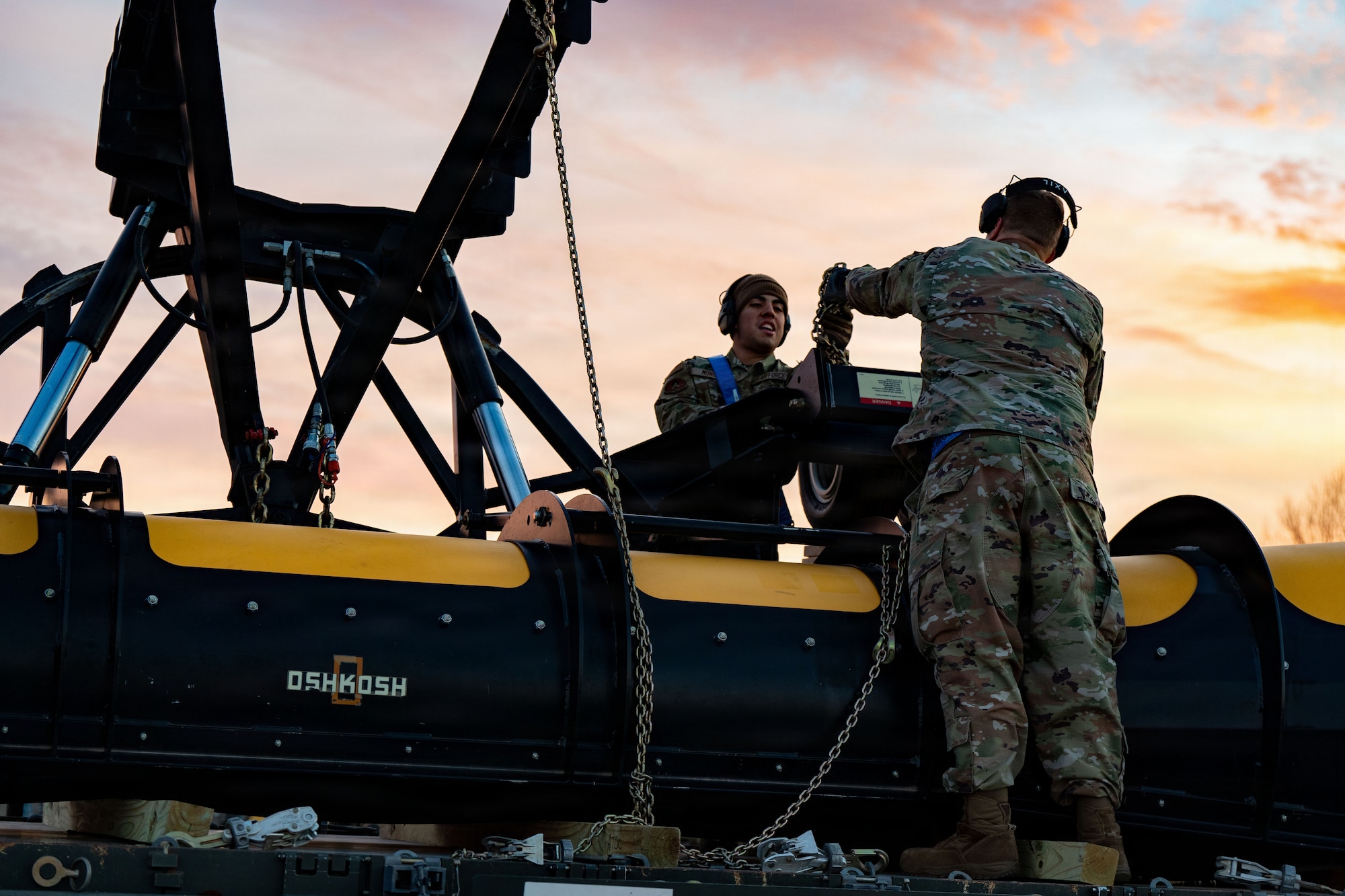 U.S. Air Force Airman 1st Class Alexander Monge, 89th Aerial Port Squadron aircraft services journeyman, receives a chain from Master Sgt. Tobi Wagner, 89th APS aircraft services superintendent, as they unload heavy snow removal equipment at Joint Base Andrews, Md., Jan. 23 2026. Air Mobility Command mobilized mission-ready Airmen and specialized equipment in support of winter weather preparedness efforts to ensure “America’s Airfield” remained operational amid historic severe weather impacts. (U.S. Air Force photo by 1st Lt. Alexis Kula)