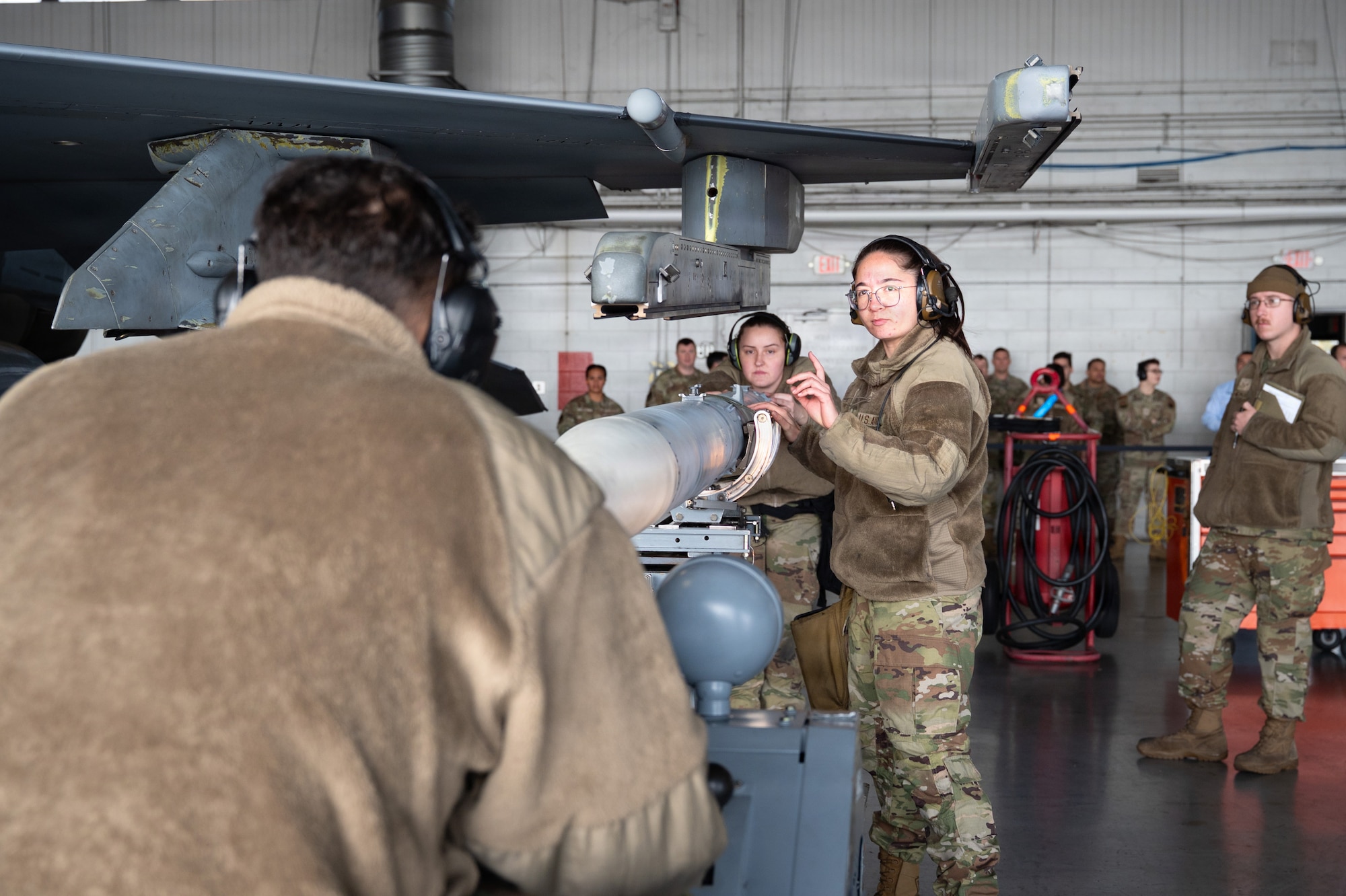 An Airman guides a missile up towards the wing of a fighter aircraft