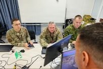 Maryland Air National Guard Lt. Col. Bob DeLuca, flight commander for the 175th Cyberspace Operations Squadron; Capt. James Bradford with the 276th Cyberspace Operations Squadron; and a member of the Estonian Defence Force speak with Maryland Air National Guard Senior Master Sgt. Martin Bartkowski, 275th Operations Support Squadron senior enlisted leader, while they participate in Crossed Swords 25 in Tallinn, Estonia, Nov. 3, 2025.