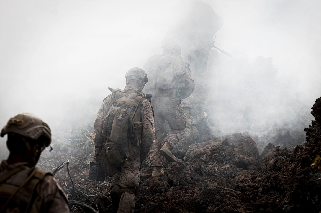 Marines in tactical gear climb a hill through fog.