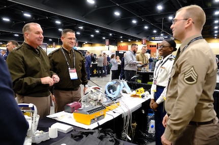 Maj. Gen. James D. Turinetti IV, left, commanding general, U.S. Army Communications-Electronics Command, and Command Sgt. Maj. Jay High, second from left, discuss medical maintenance operations with Staff Sgt. Charles Roberts and Sgt. Kimberli McDonald, of U.S. Army Medical Logistics Command AMLC’s Medical Maintenance Operations Division at Hill Air Force Base, Utah, during the 2025 Department of War Maintenance and Logistics Exhibition at the Phoenix Conference Center, Jan. 21, 2026.