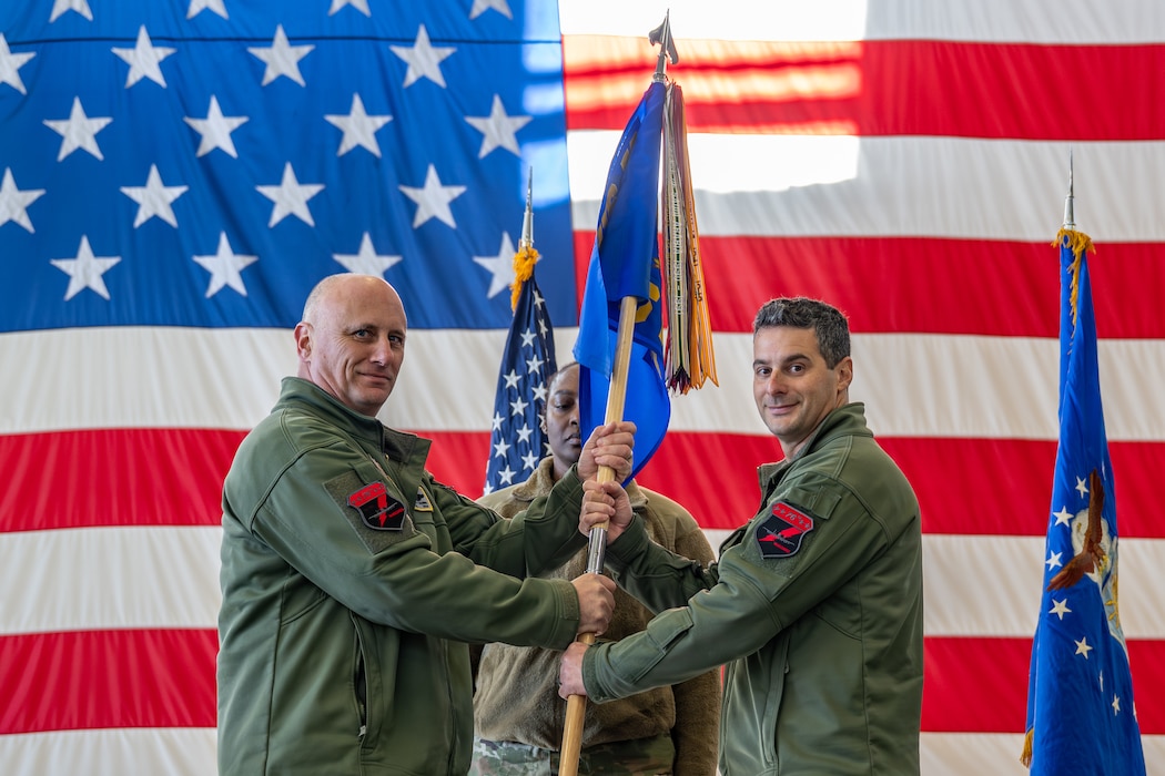 U.S. Air Force Col. Brett Waring, left, 476th Fighter Group commander, passes the guidon to Lt. Col. Stephen McNamara, right, 76th Fighter Squadron commander, during a change of command ceremony.