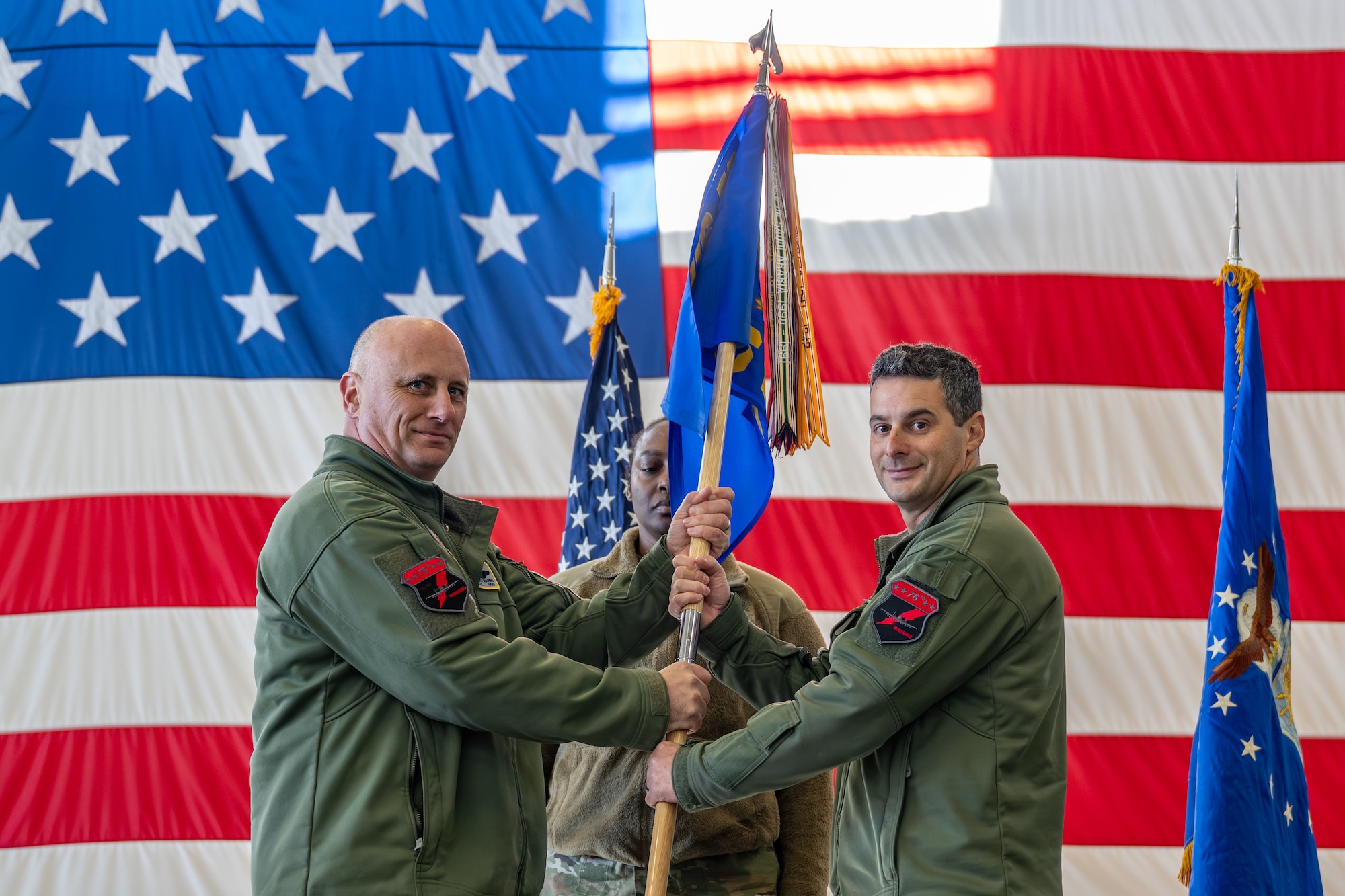 U.S. Air Force Col. Brett Waring, left, 476th Fighter Group commander, passes the guidon to Lt. Col. Stephen McNamara, right, 76th Fighter Squadron commander, during a change of command ceremony.