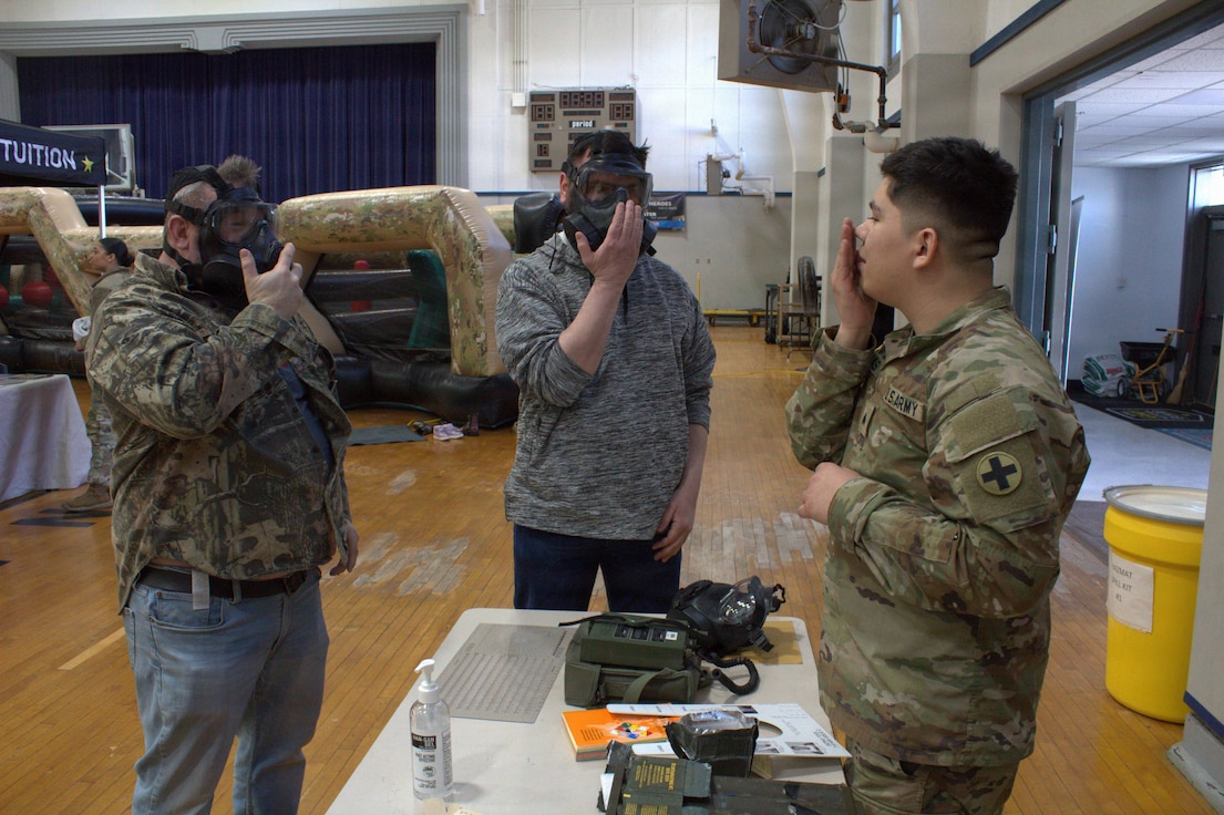 Sgt. Juan Carlos Vargas demonstrates to Donnie Spaniol (center) and Mike Miller (left) how to ensure that they have a good seal while wearing an M50 gas mask at the Sycamore Armory.