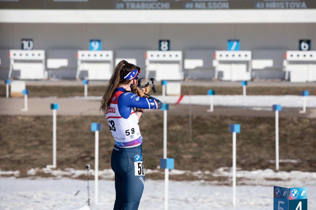 A woman wearing ski sports gear aims a rifle at a target.