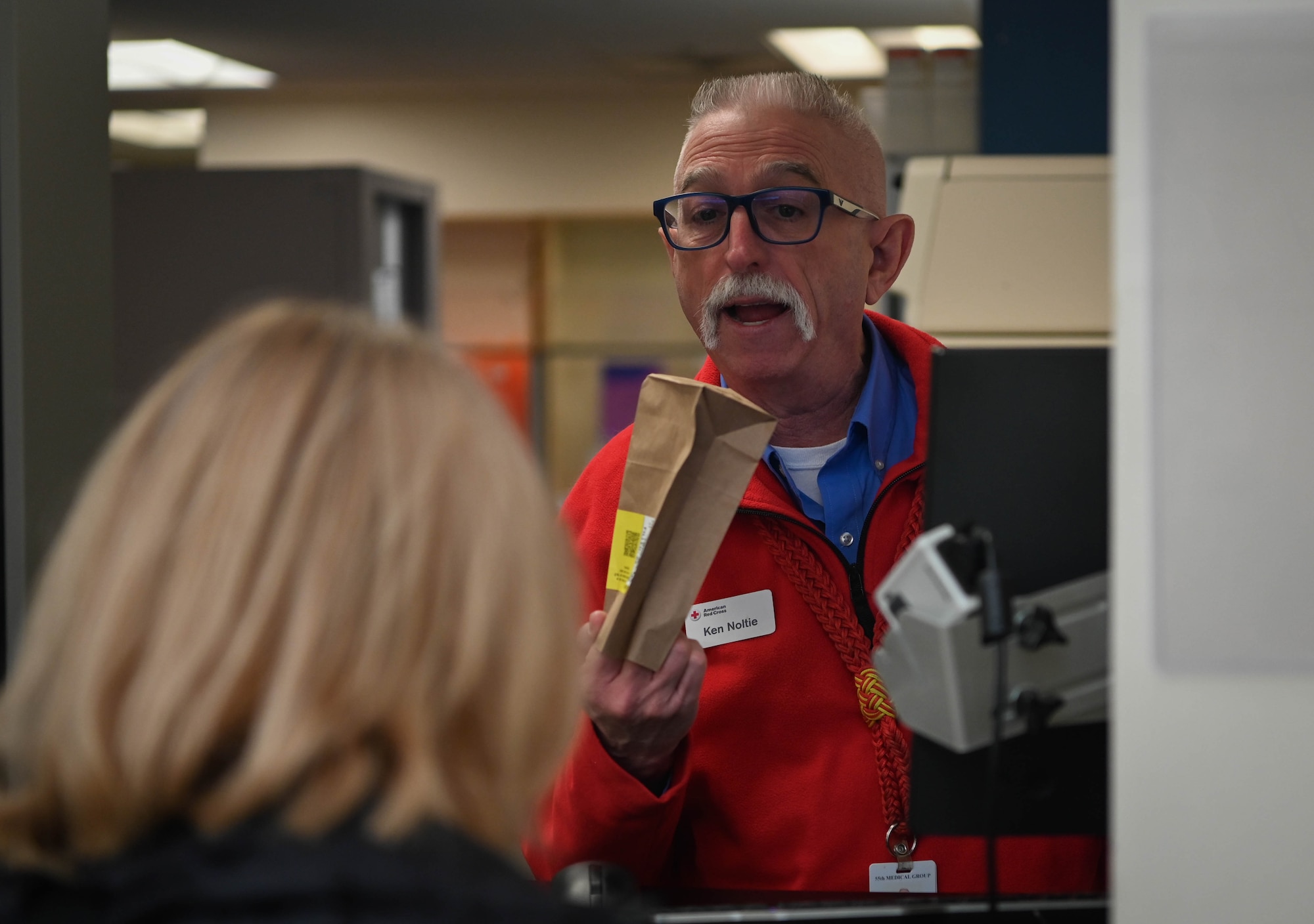 Ken Noltie, Red Cross volunteer lead, assists a customer at the Ehrling Bergquist Clinic pharmacy located at the 55th Medical Group facility, January 9, 2026. Noltie recruits volunteers primarily to assist in pharmacy operations to ease the workload demands for active-duty medical personnel. (U.S. Air Force photo by Daniel Martinez)