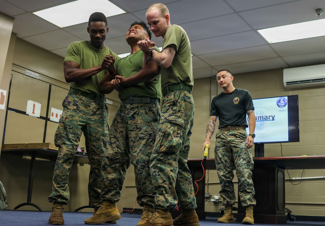 U.S. Marine Corps Lance Cpl. Sharden Valentine, middle, operations and training administrative specialist, Headquarters and Service Battalion, U.S. Marine Corps Forces, Pacific, takes part in the taser test during a Security Augmentation Force class at Camp H.M. Smith, Hawaii, Jan. 29, 2026. SAF training prepares Marines to respond swiftly and effectively to real-world security threats, ensuring the protection of personnel, assets, and mission-critical operations. (U.S. Marine Corps photo by Lance Cpl. Roger-Junior Annoh)