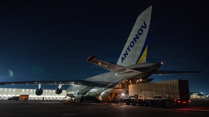 Airman push a container into the back of an open aircraft on a dark flight line.