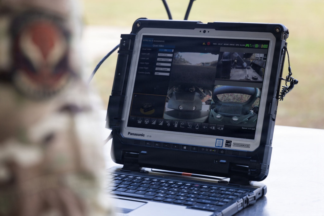 A person in a camouflage military uniform looks at a computer screen that displays the live view from multiple drones.