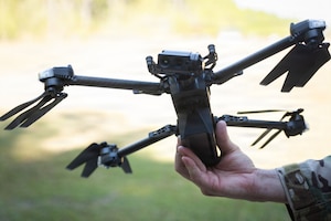 A close-up view of a drone as it's held by a person in a camouflage uniform.