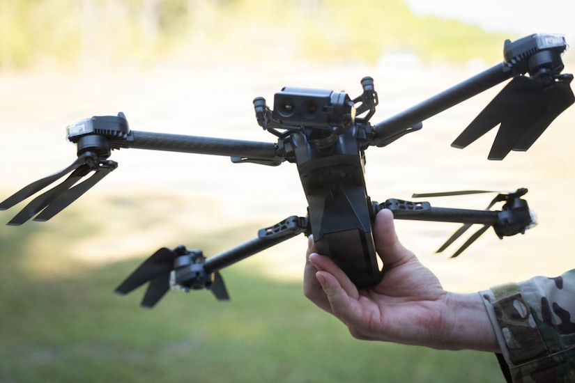 A close-up view of a drone as it’s held by a person in a camouflage military uniform.