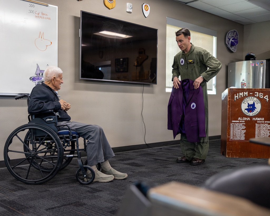 U.S. Marine Corps Lt. Col. Bunce, commanding officer of Marine Medium Tiltrotor Squadron (VMM) 364, Marine Aircraft Group 39, 3rd Marine Aircraft Wing, gifts U.S. Marine Corps veteran, Capt. Nelson J. Baker, an honorary Purple Foxes jacket at Marine Corps Air Station Camp Pendleton, California, Jan. 30, 2026. Baker is a plank holder of VMM-364 and served as one of the squadron’s first pilots when it was commissioned as Marine Medium Helicopter Squadron (HMM) 364 in 1961. He visited to share the squadron’s legacy with the current generation of Marines who work with and fly the MV-22B Osprey. (U.S. Marine Corps photo by Lance Cpl. Jonathan Sherchand)