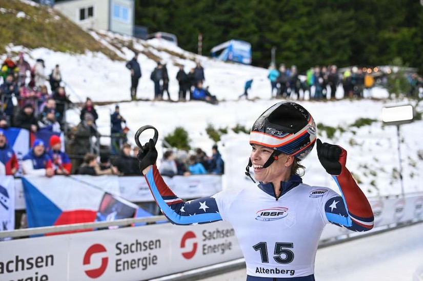 A woman wearing winter Olympic gear cheers in front of a crowd.