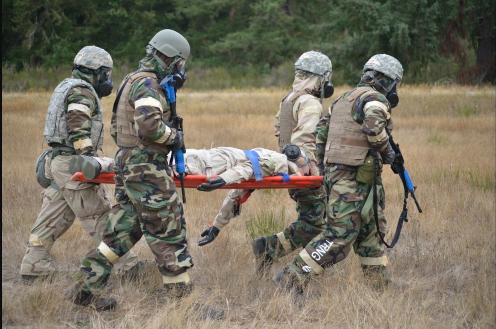 Four men in military uniform carry a patient in a field.