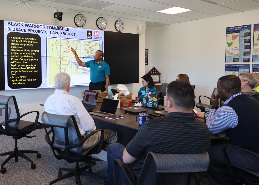 People sitting around a table while a man give a presentation.