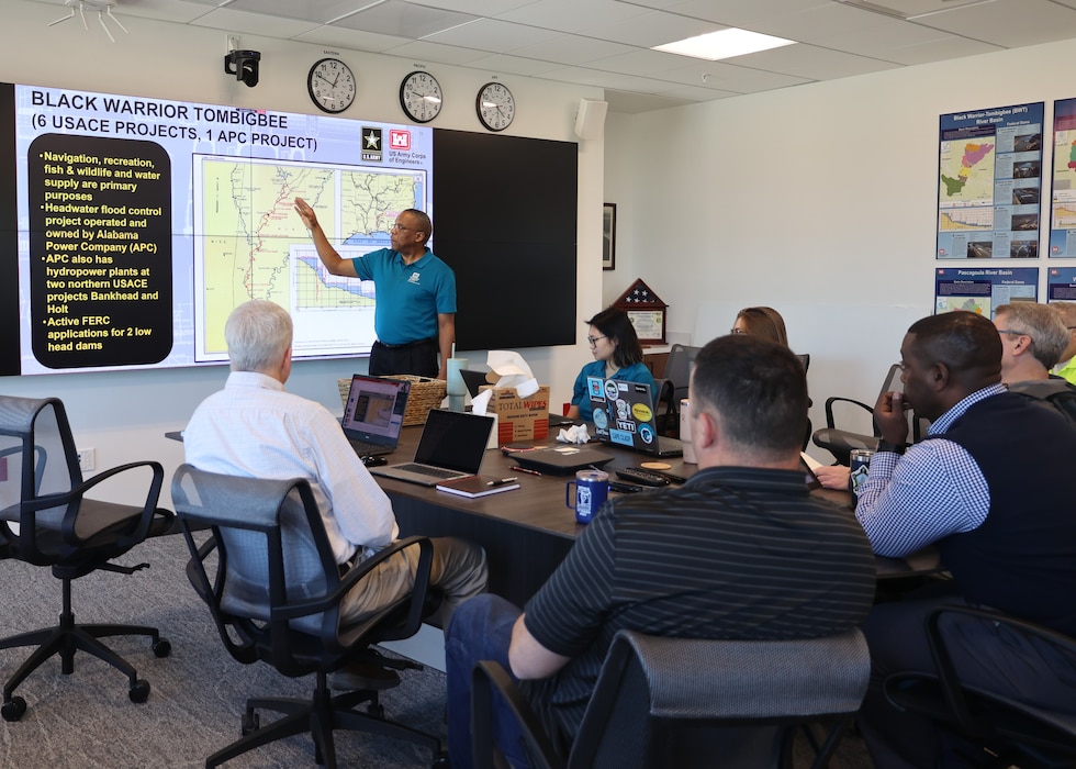 People sitting around a table while a man give a presentation.