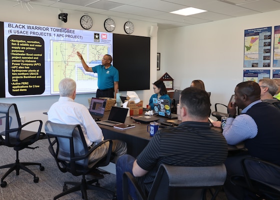 People sitting around a table while a man give a presentation.