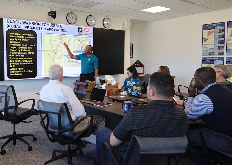 People sitting around a table while a man give a presentation.