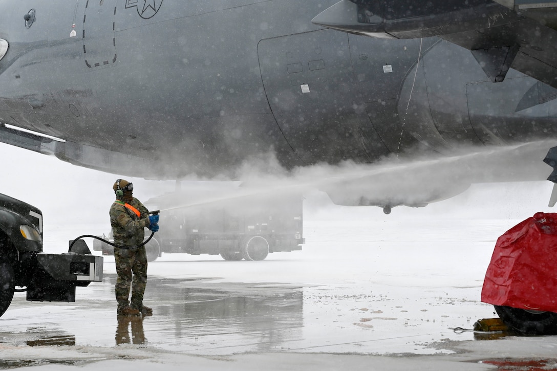 Steam fills the air as an airman uses a hose to deice an aircraft on a blustery, cold day.