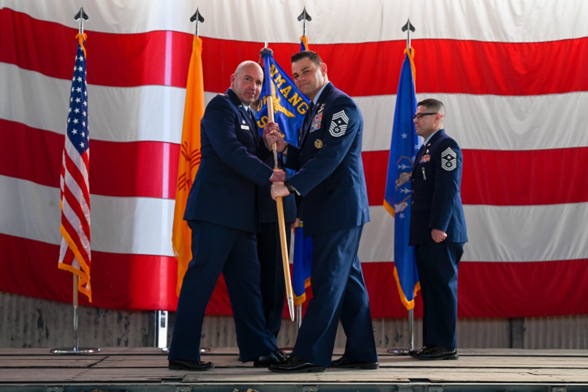 Two Airmen in Air Force dress uniforms hold a guidon on stage during an official ceremony.