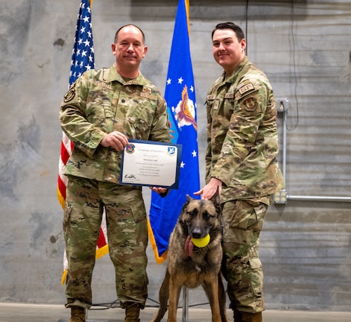 Lt. Col. Kevin Collett, 88th Security Forces Commander, SrA Devan Hiler, 88th Security Forces Dog Handler join Military Working Dog “Flex” to celebrate the start of his retirement Feb. 9, 2026 at Wright-Patterson Air Force Base, Ohio, after serving for six and a half years. (U.S. Air Force by Jack Gardner)