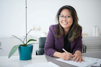 Smiling woman wearing glasses sits at table with potted plant.