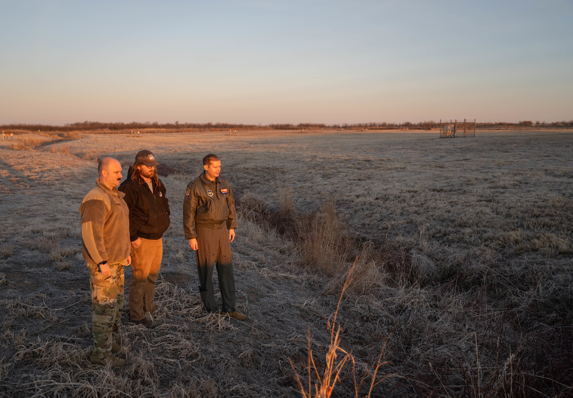 U.S. Air Force Chief Master Sgt. Jonny Adams, 97th Air Mobility Wing (AMW) command chief, left, Mitchell Singer, U.S. Department of Agriculture wildlife biologist, center, and U.S. Air Force Col. Richard Kind, 97th AMW commander, right, observe a drainage ditch at Altus Air Force Base, Oklahoma, Feb. 5, 2026. Throughout the immersion tour, Singer highlighted specific areas of concern such as 10-foot drainage ditches, essential for water management, yet attractive hiding spots for small wildlife that can quickly become a danger during flight operations. (U.S. Air Force photo by Airman 1st Class Emma Wright)