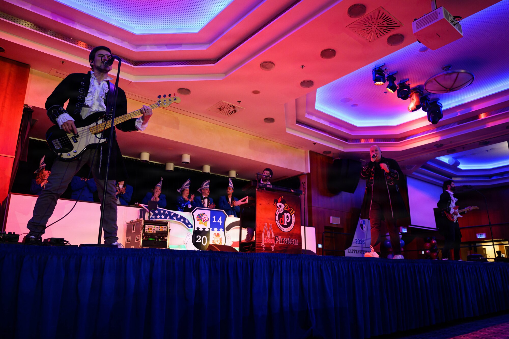 A small band plays music on a stage inside a ballroom.
