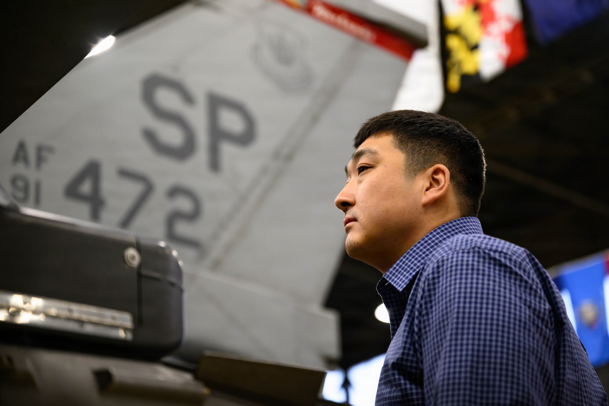 A person looks at a fighter aircraft inside of an aircraft hangar.