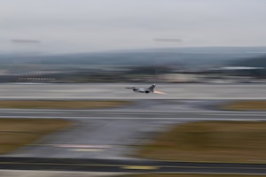 A fighter aircraft takes off from a runway at an air base.