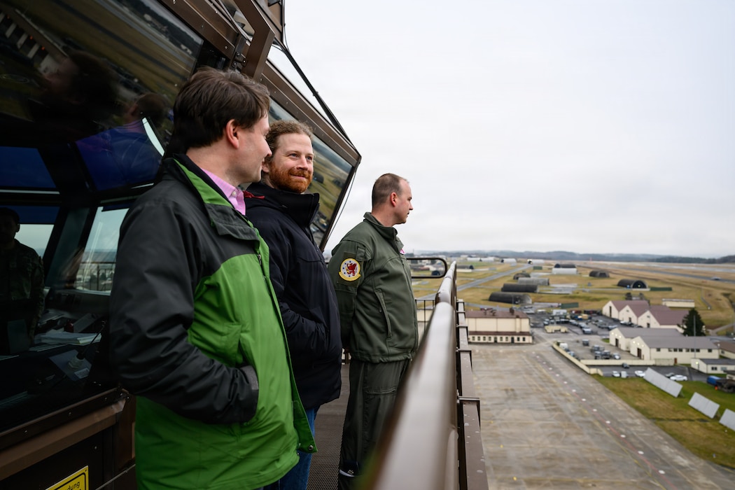 A group of people look out across an air base from atop an air traffic control tower.