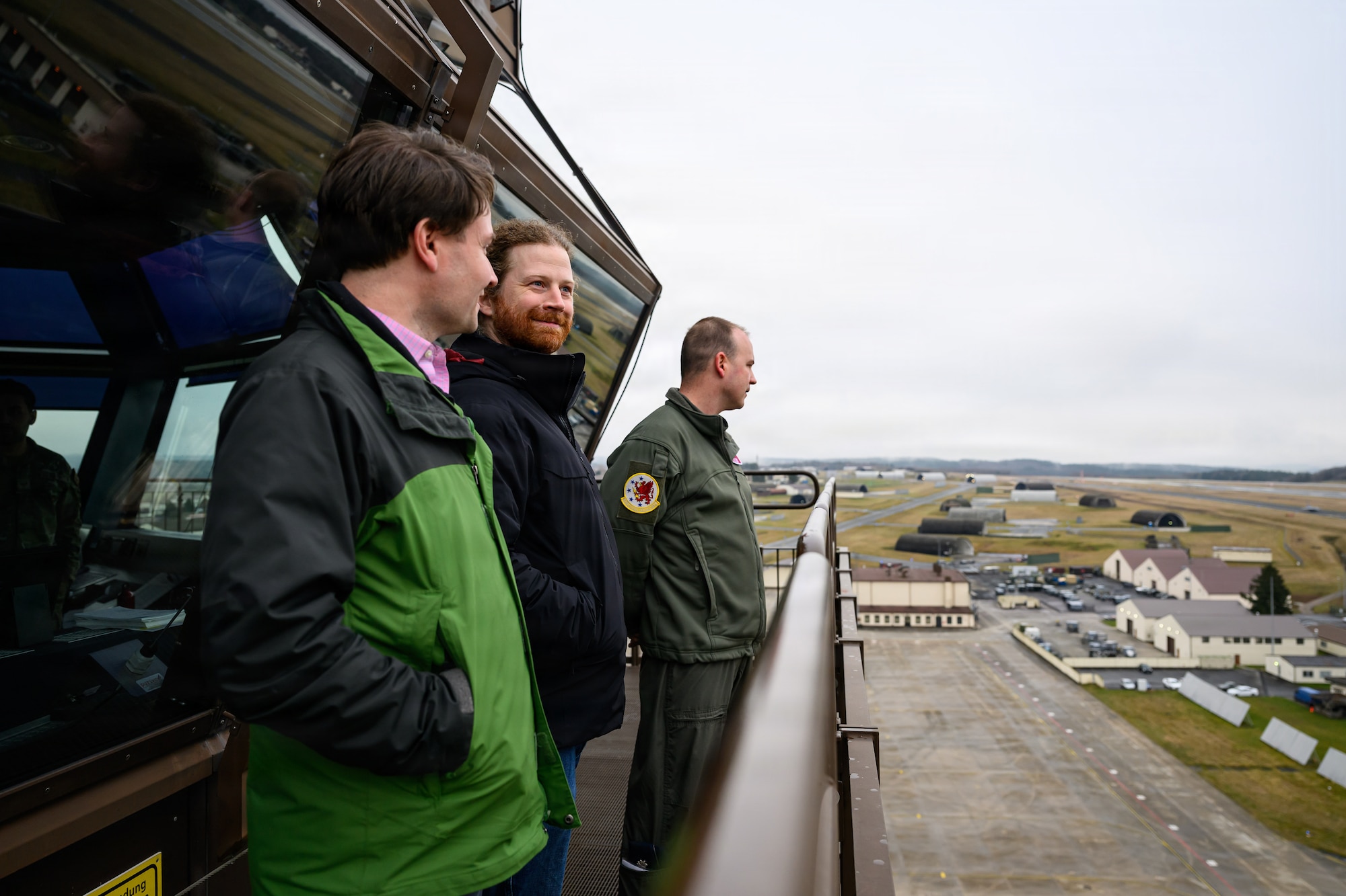 A group of people look out across an air base from atop an air traffic control tower.