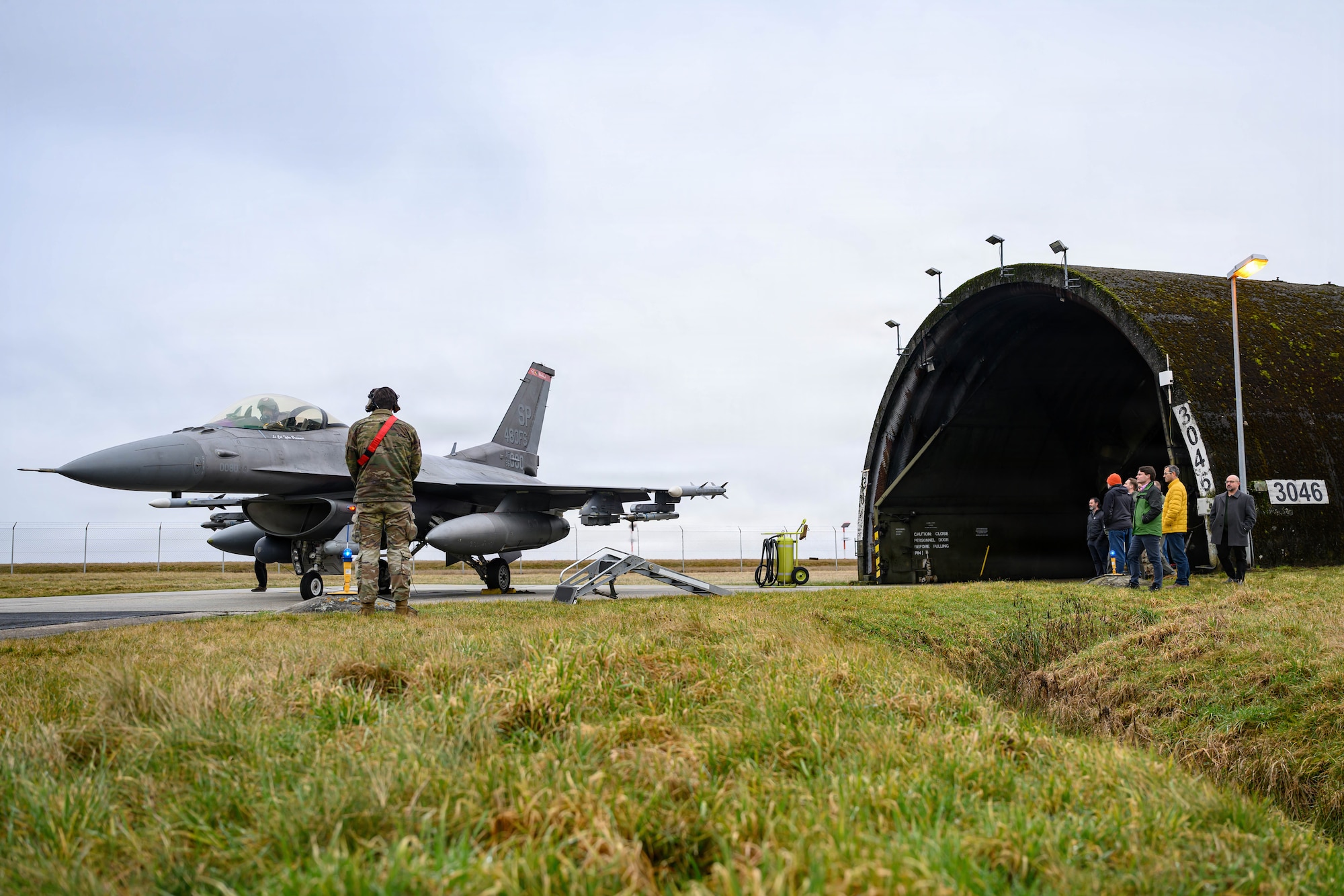 A group of people watch a team of aircraft maintainers prepare an aircraft for flight.