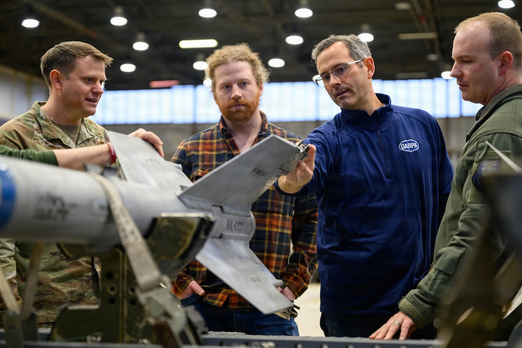 Four people have a discussion around a missile sitting on a cart.