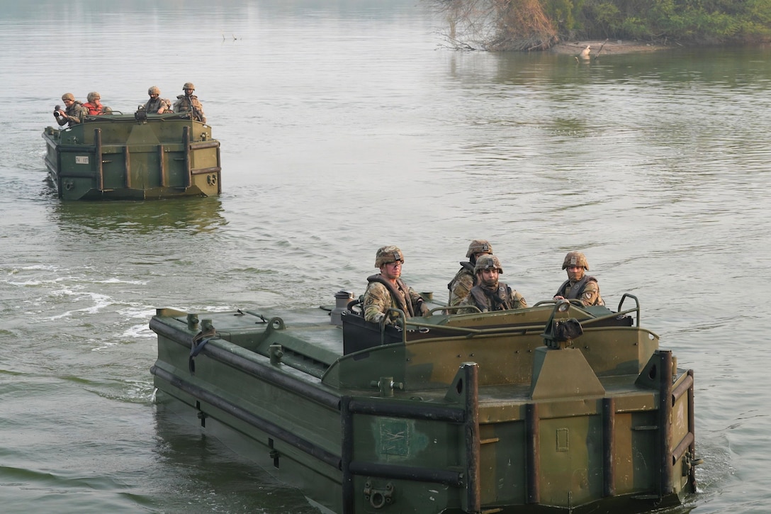Soldiers operate two small boats in a murky river.