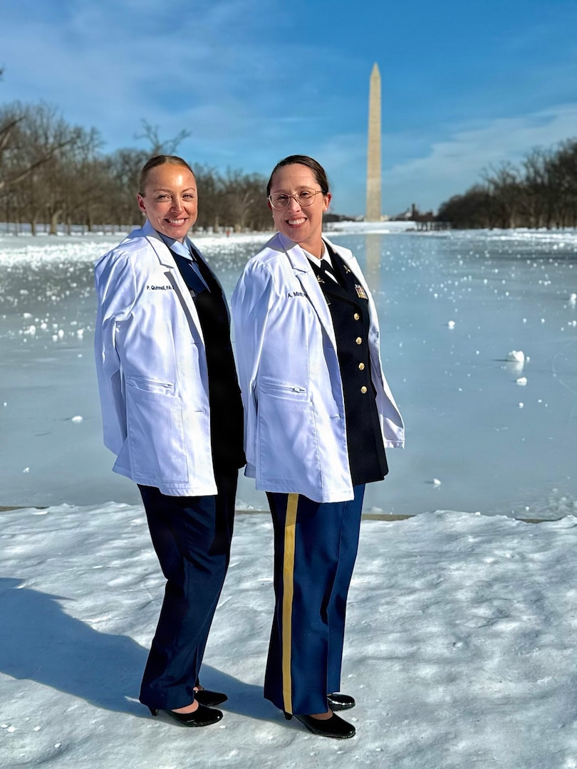 Two women service members wearing their white coats smile while standing next to each other.