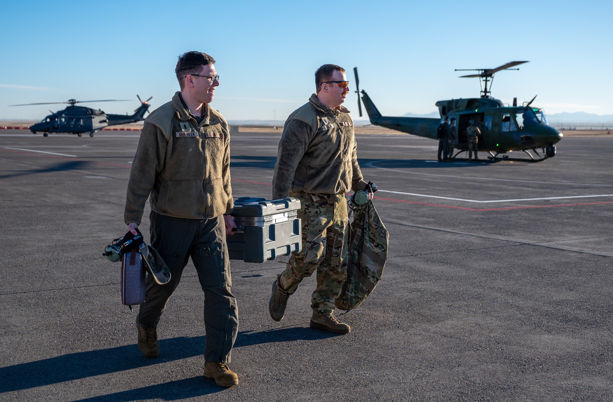 Two uniformed men carry a case to a helicopter.