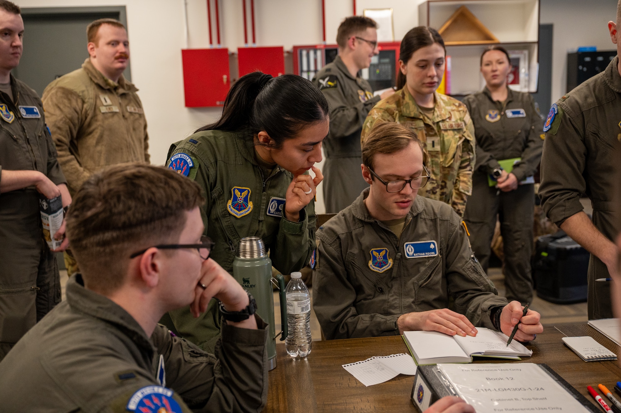 A woman in uniform leans over a man in uniform's shoulder.
