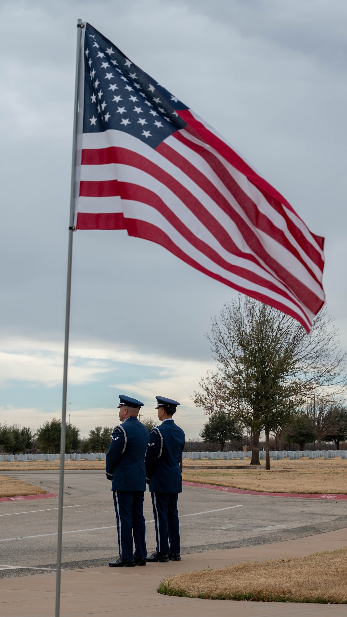 U.S. Air Force Airman 1st Class Jovel Galindo, left, and U.S. Air Force Airman 1st Class Nickey Phanhsopha, both 7th Force Support Squadron ceremonial guardsmen, stand in silence as they await the arrival of family members during a funeral service at the Texas State Veterans Cemetery in Abilene, Texas, Jan. 13, 2026. Airmen from a variety of career fields volunteer to serve on the Dyess Honor Guard, safeguarding the traditions of the Air Force and honoring those who served before them. (U.S. Air Force photo by Airman William Neal)
