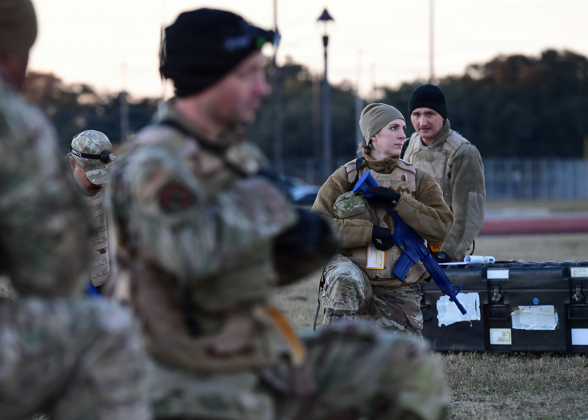 A woman in military gear stands outside during a training scenario.